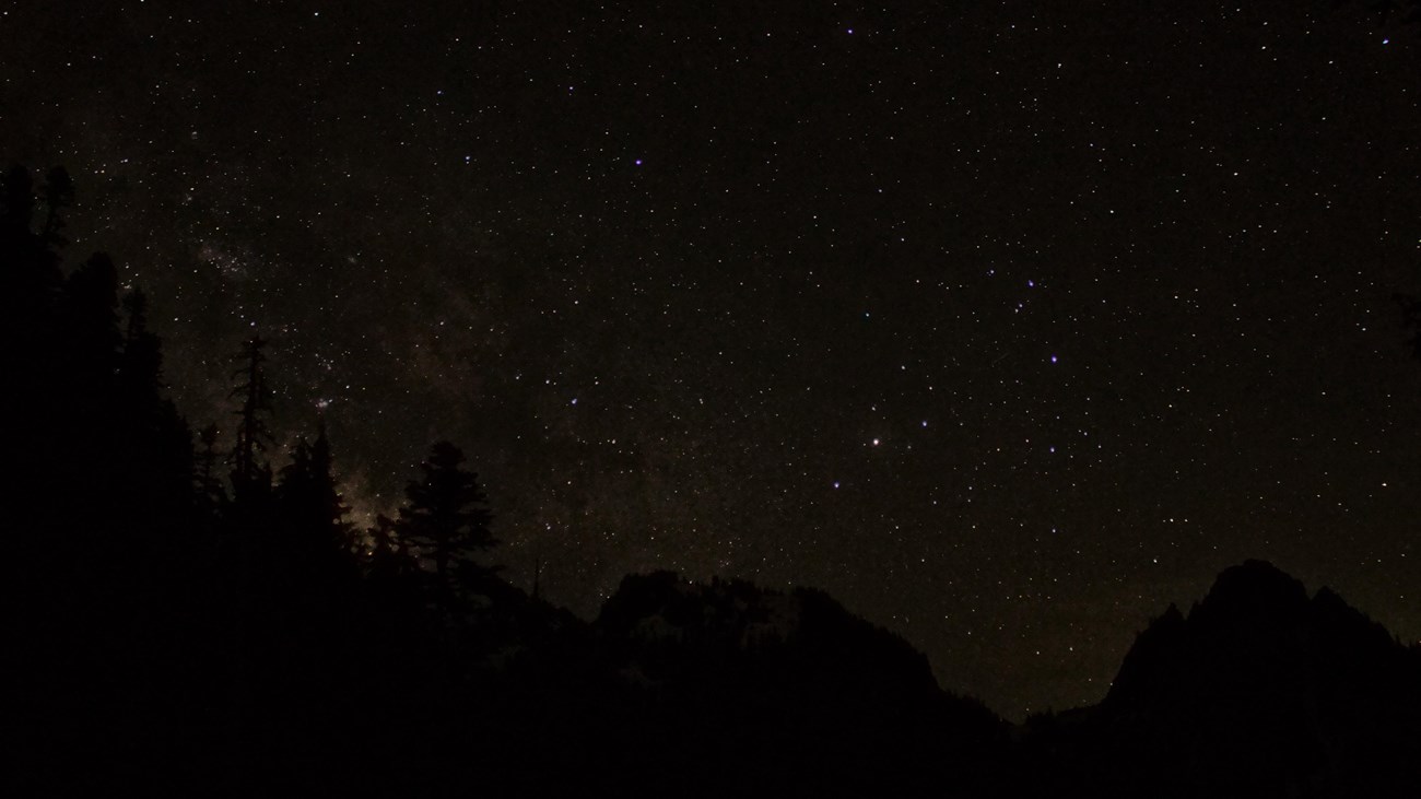 A starry night sky above a ridge of rocky mountain peaks.