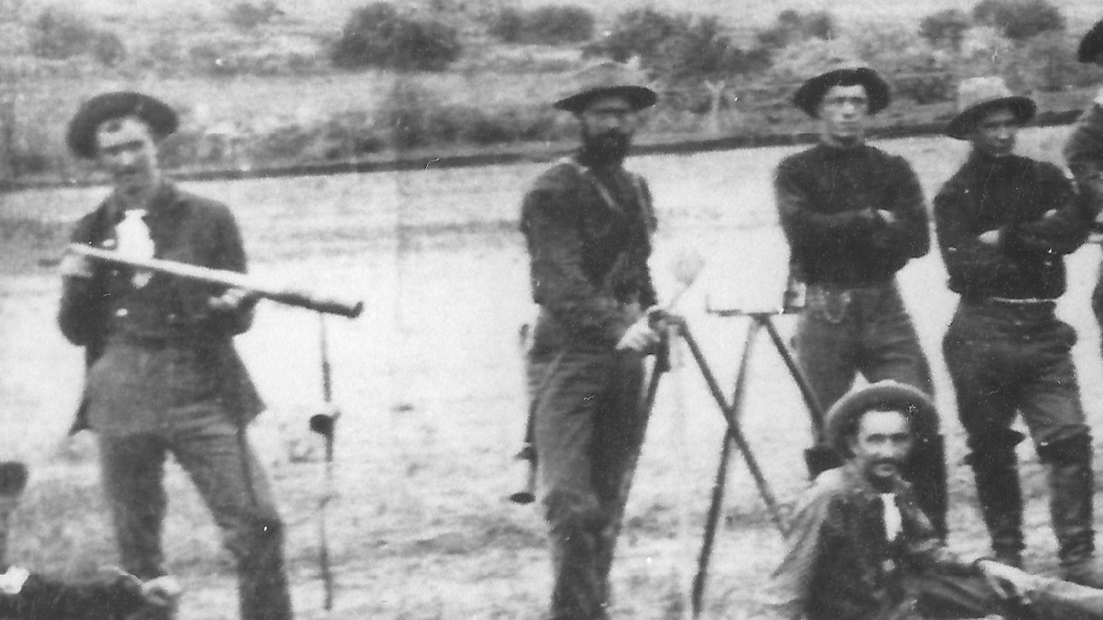 An historic black and white image. Men in uniform, hold signaling equipment, with tents behind them.