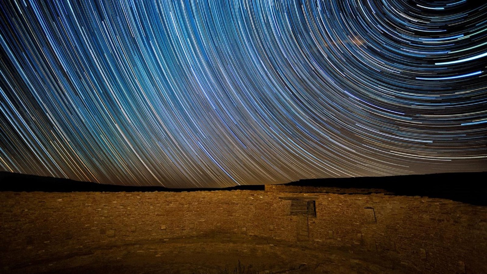 A time lapse photo shows star trails across the sky over the great kiva Casa Rinconada.
