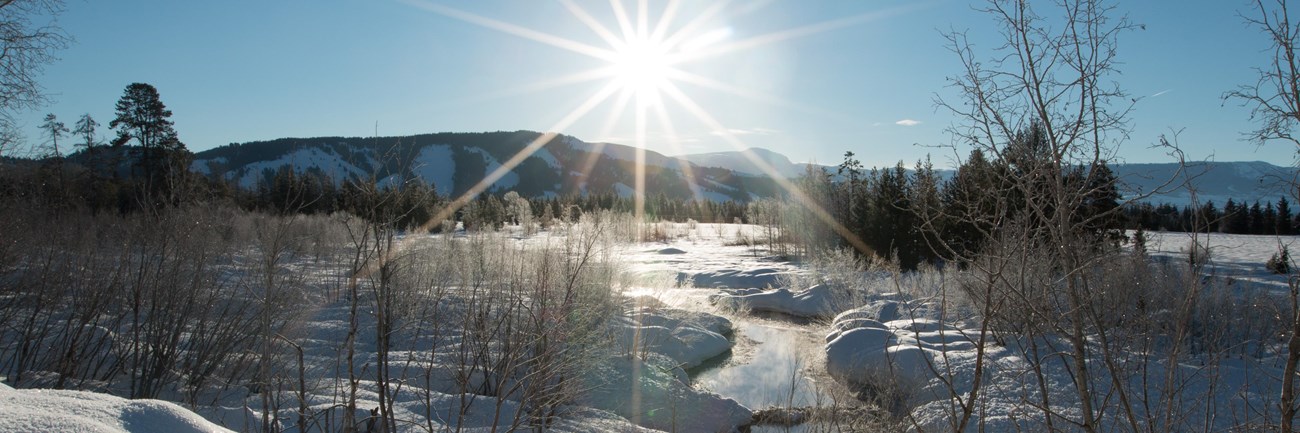 Sunlit blue sky with a meandering creek running through a snow and ice covered marsh.