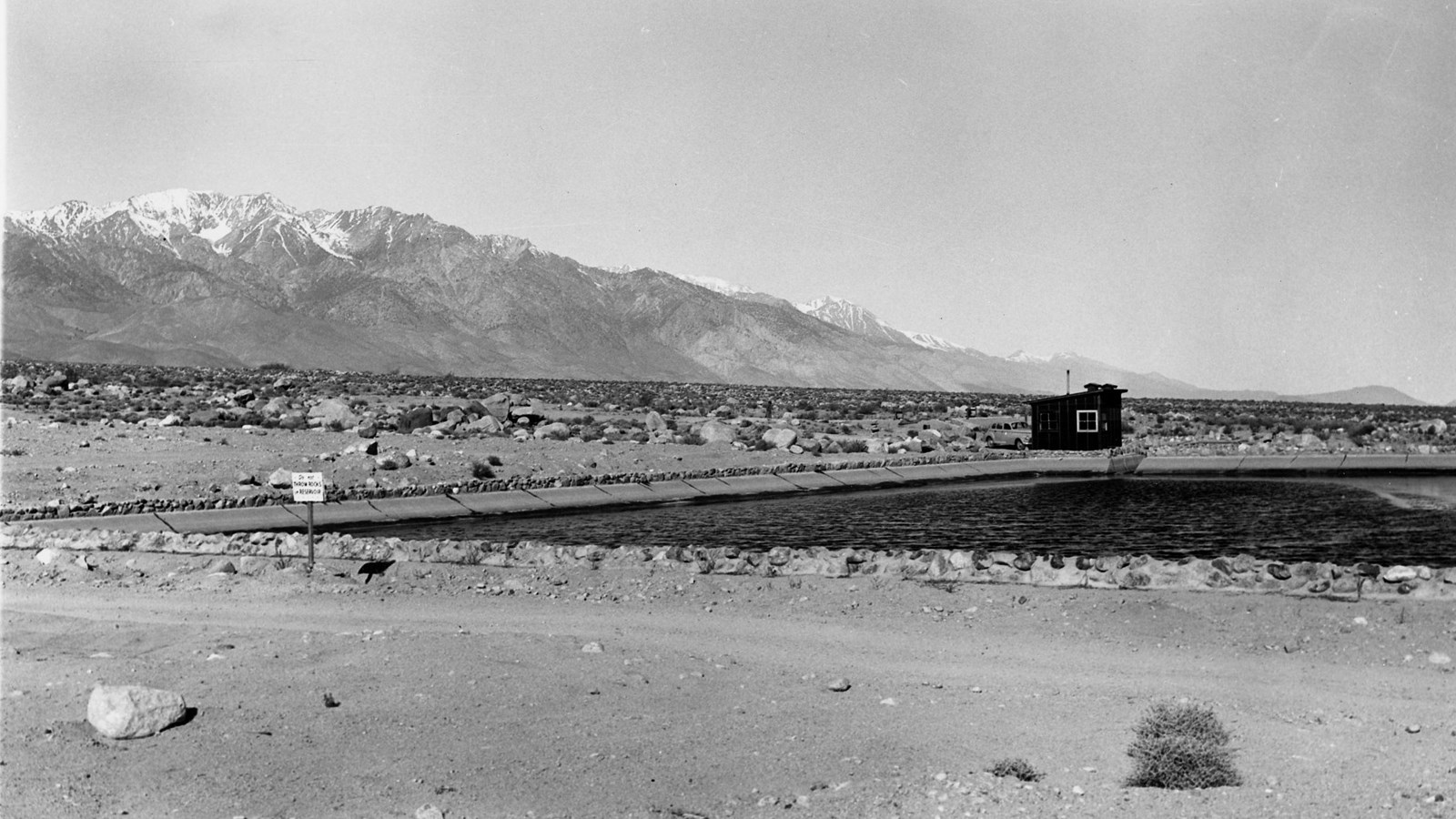 Black and white photo of reservoir filled with water and small support building
