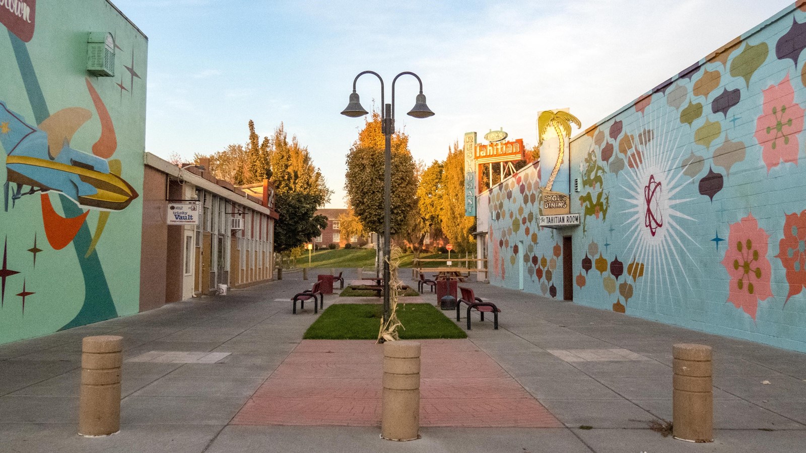 Color photo of a concrete atrium lined with benches. On both sides are colorful murals.