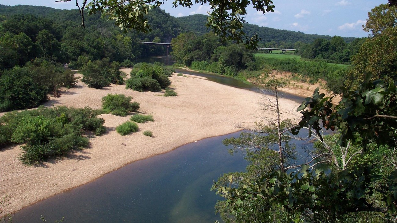 view from above of trees and river at right and tan gravel and trees at left.