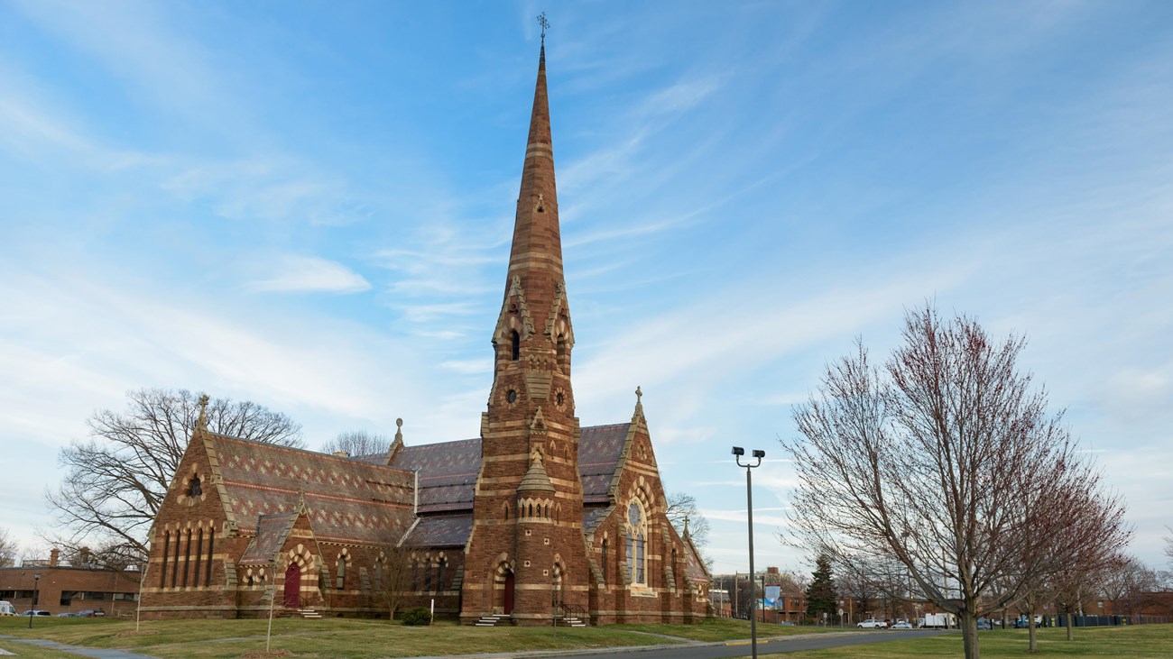 A church with green grass and bare trees in front against a blue sky.