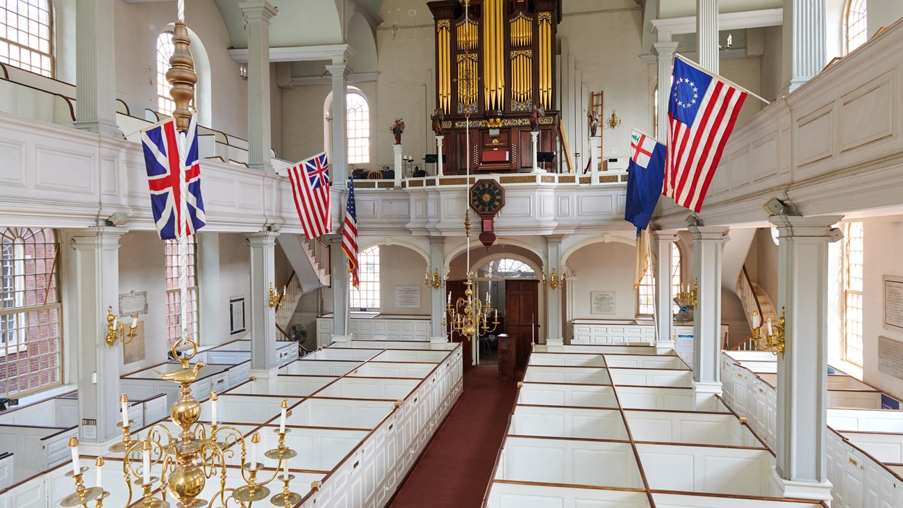 Interior of Old North Church with box pews and flags hanging from the gallery.