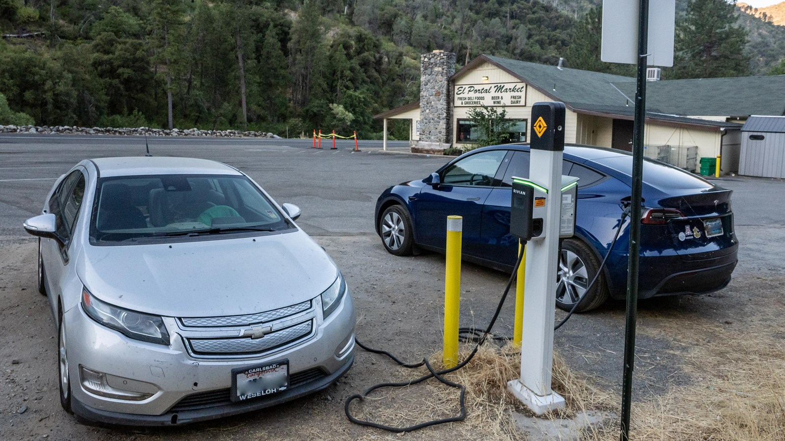 Two electric vehicles plugged into a charging station in a parking area