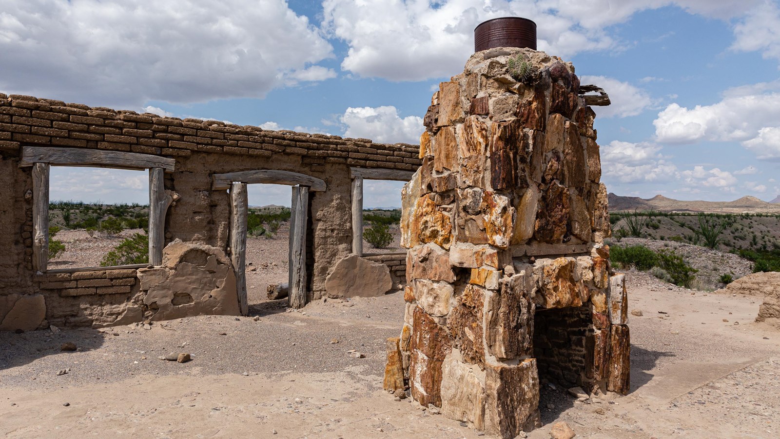 An adobe wall and a petrified wood chimney rest up on a mesa above the surrounding desert.