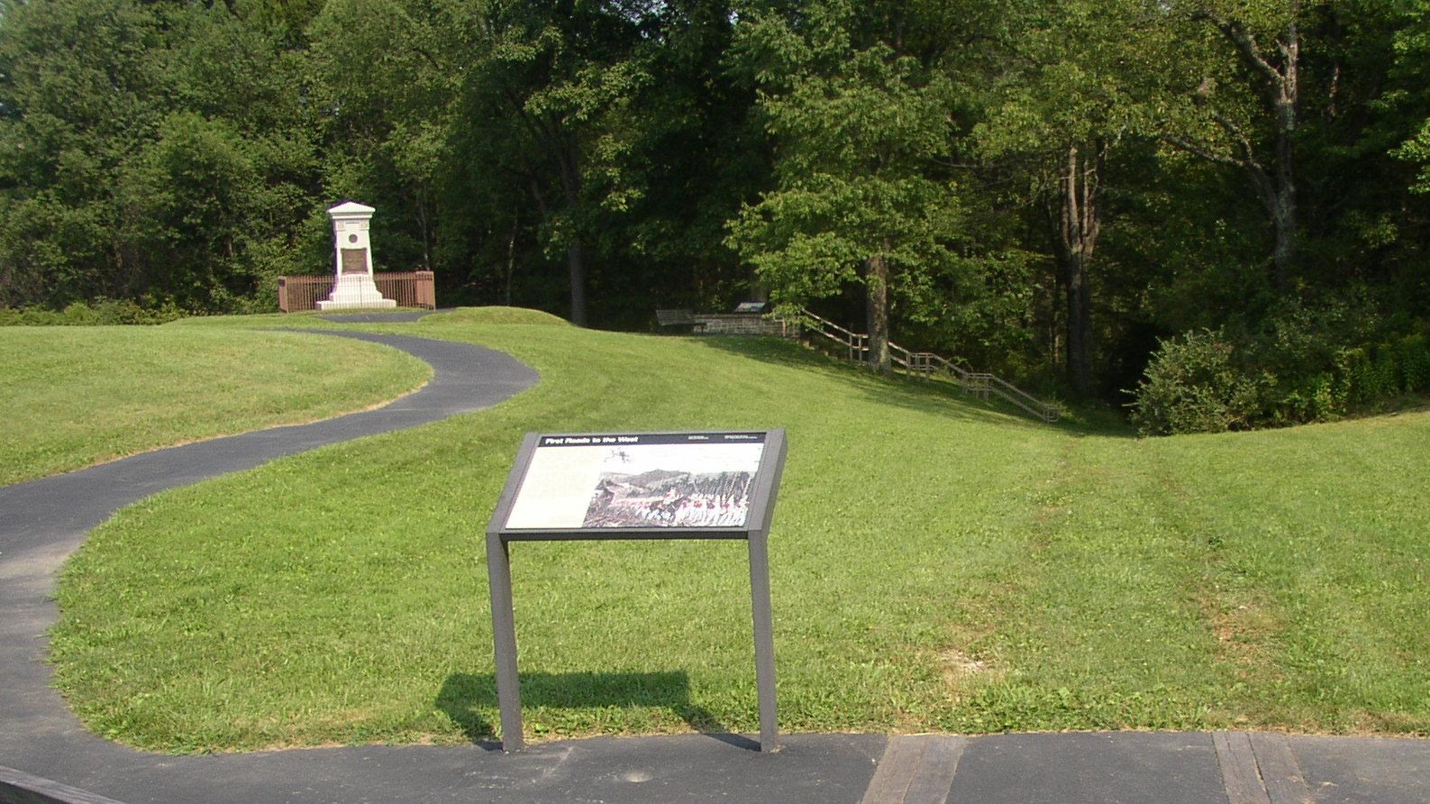 A white monument in the background with an interpretive sign in the foreground