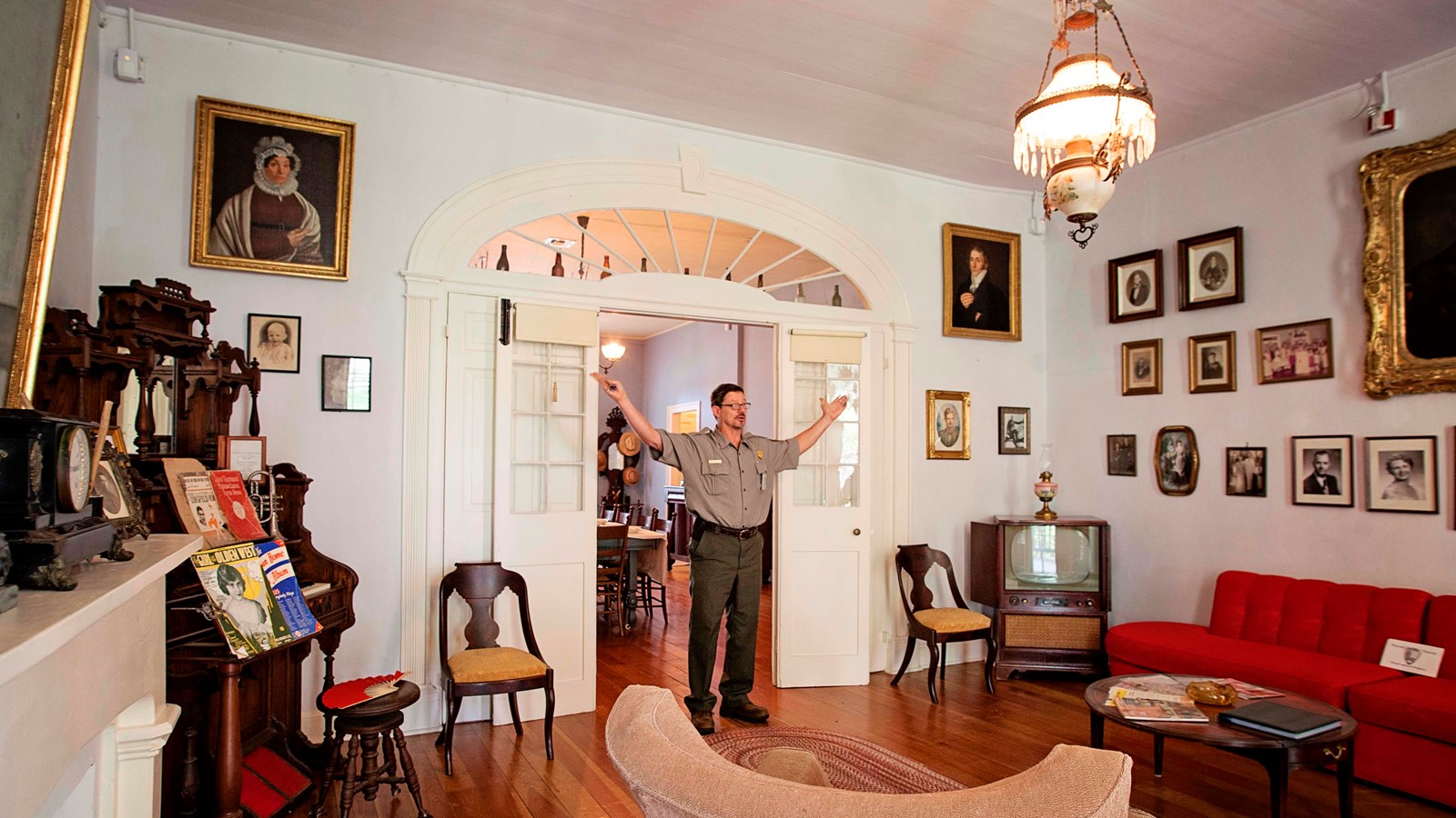 A ranger stands in the doorway between the parlor and the dining room surrounded by furniture.