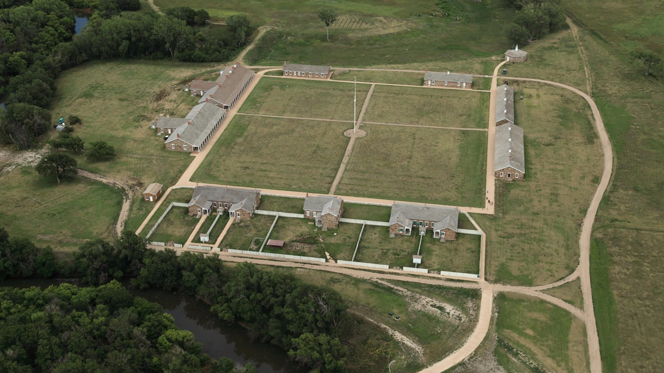 Aerial view of sandstone buildings arranged in a square around an open grassy area.