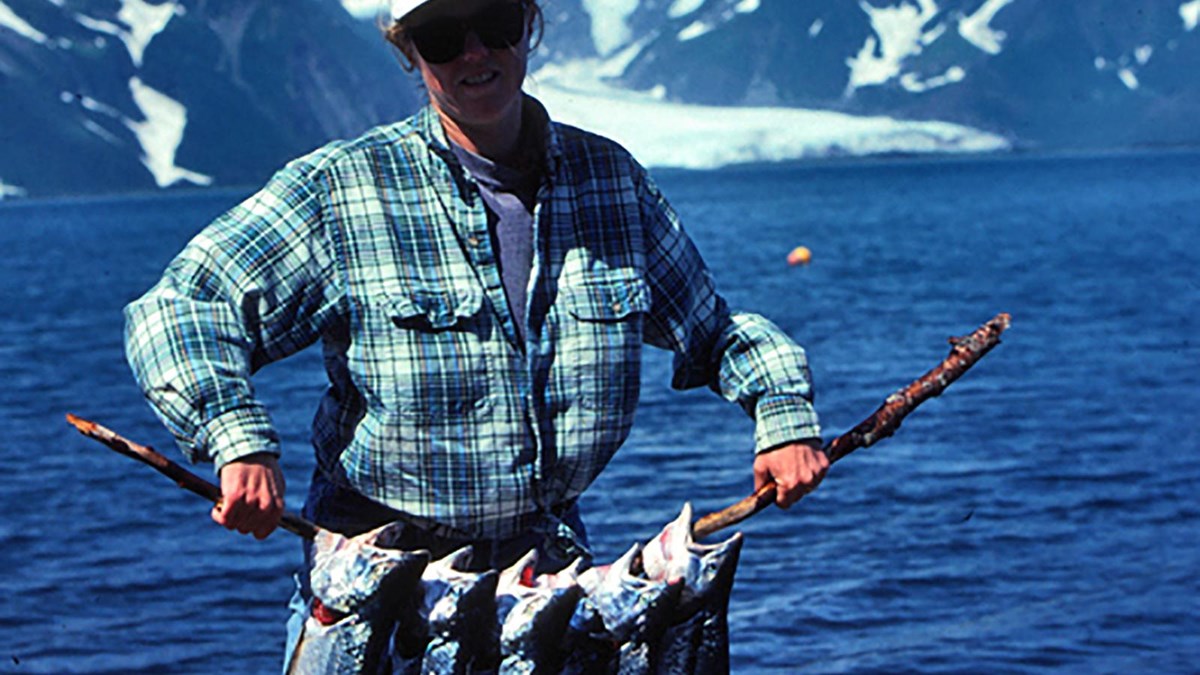 A man holding a stick with six salmon hanging from the stick.