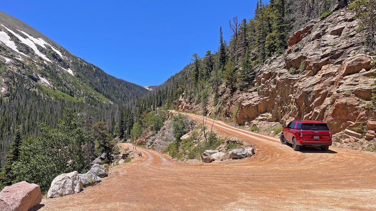 A small SUV is driving on the dirt, narrow switchbacks on Old Fall River Road