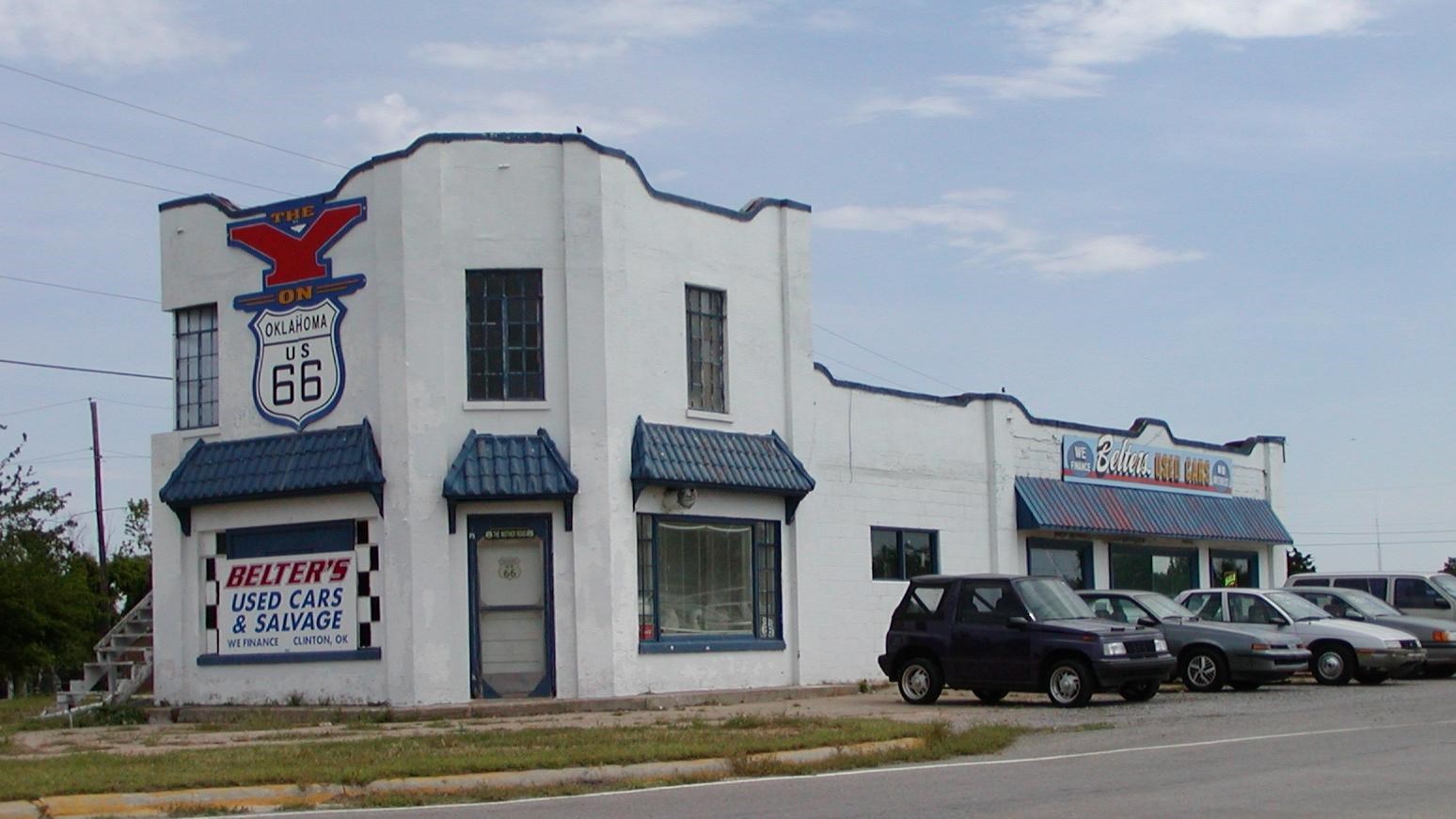 A two story white building with blue trim and awnings over the windows. On the side is a red 