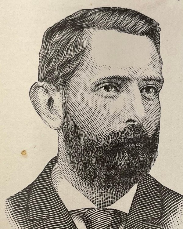 A man with a dark beard, suit jacket and tie.