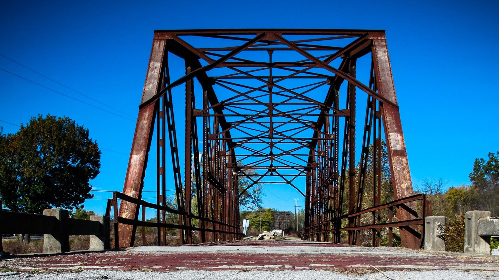 A road with a Route 66 logo leads up to a rusted steel-truss bridge.
