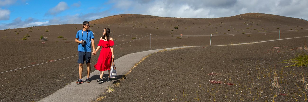 Two people holding hands on a paved path through a cinder-covered landscape