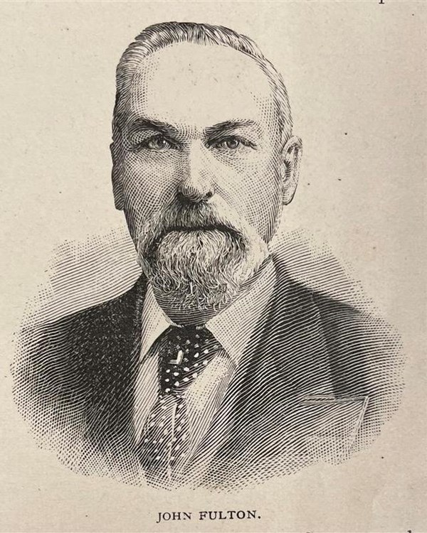 A man with a gray beard and a dark suit jacket and tie.