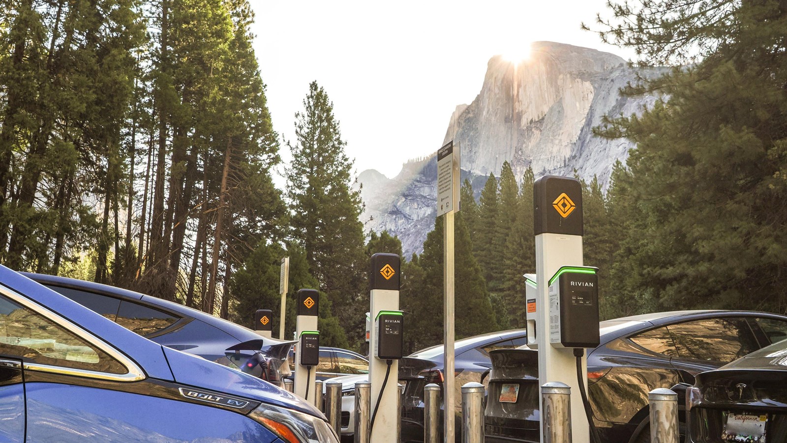 Several vehicles charging in a parking lot with Half Dome towering in the background