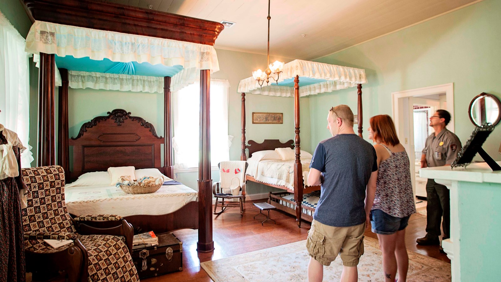 A ranger and two visitors stand in the girls\' room which features two large beds from the 1830s.
