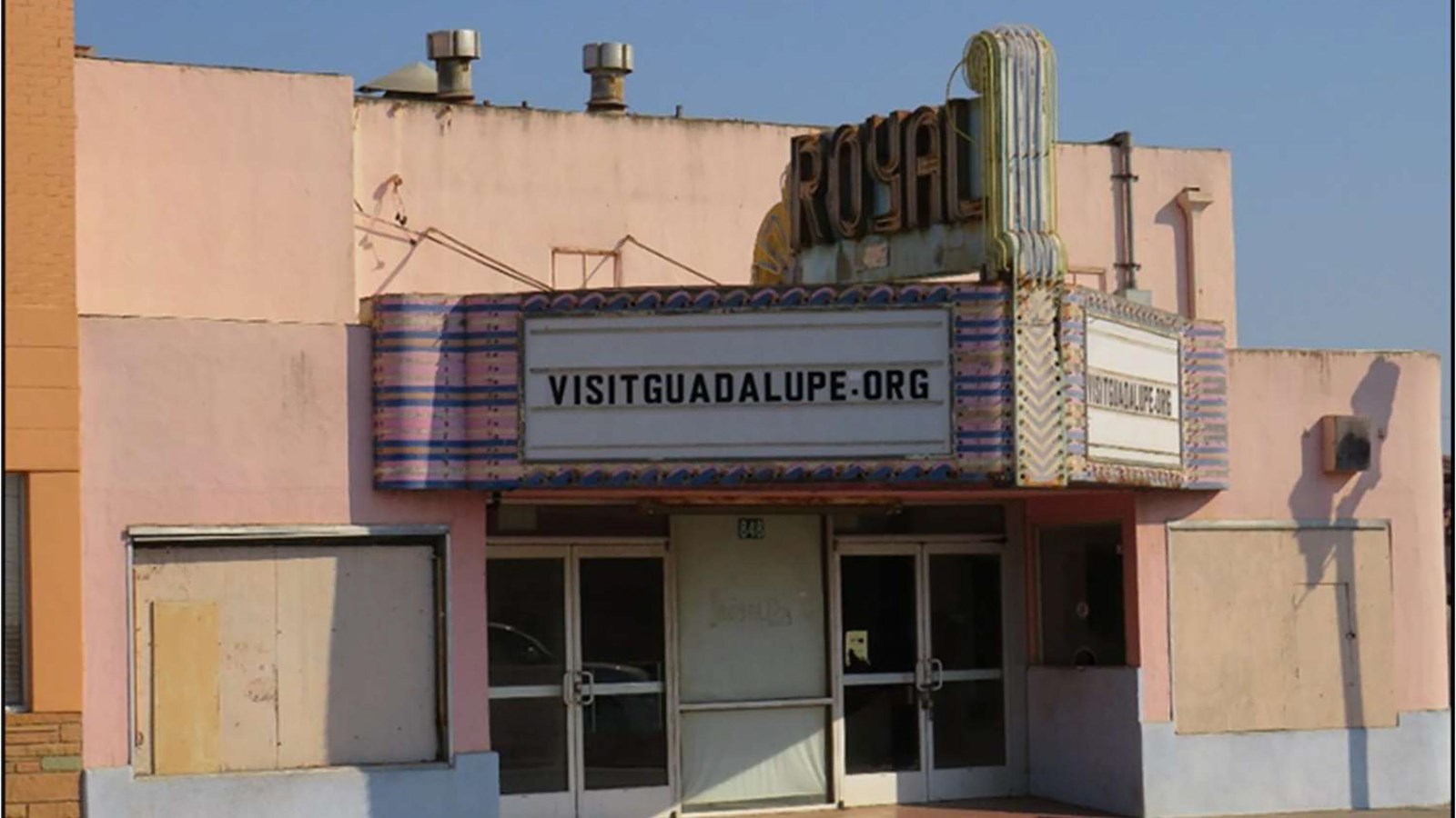 Theater entrance with Art Deco Sign reading Royal, and marquee reading visitguadalupe.org
