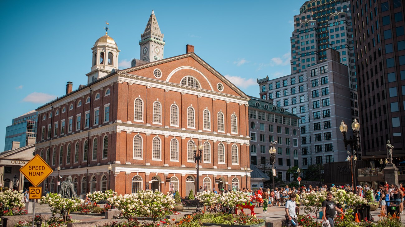 Three story brick building with white furnishes and a white and gilded cupola atop.