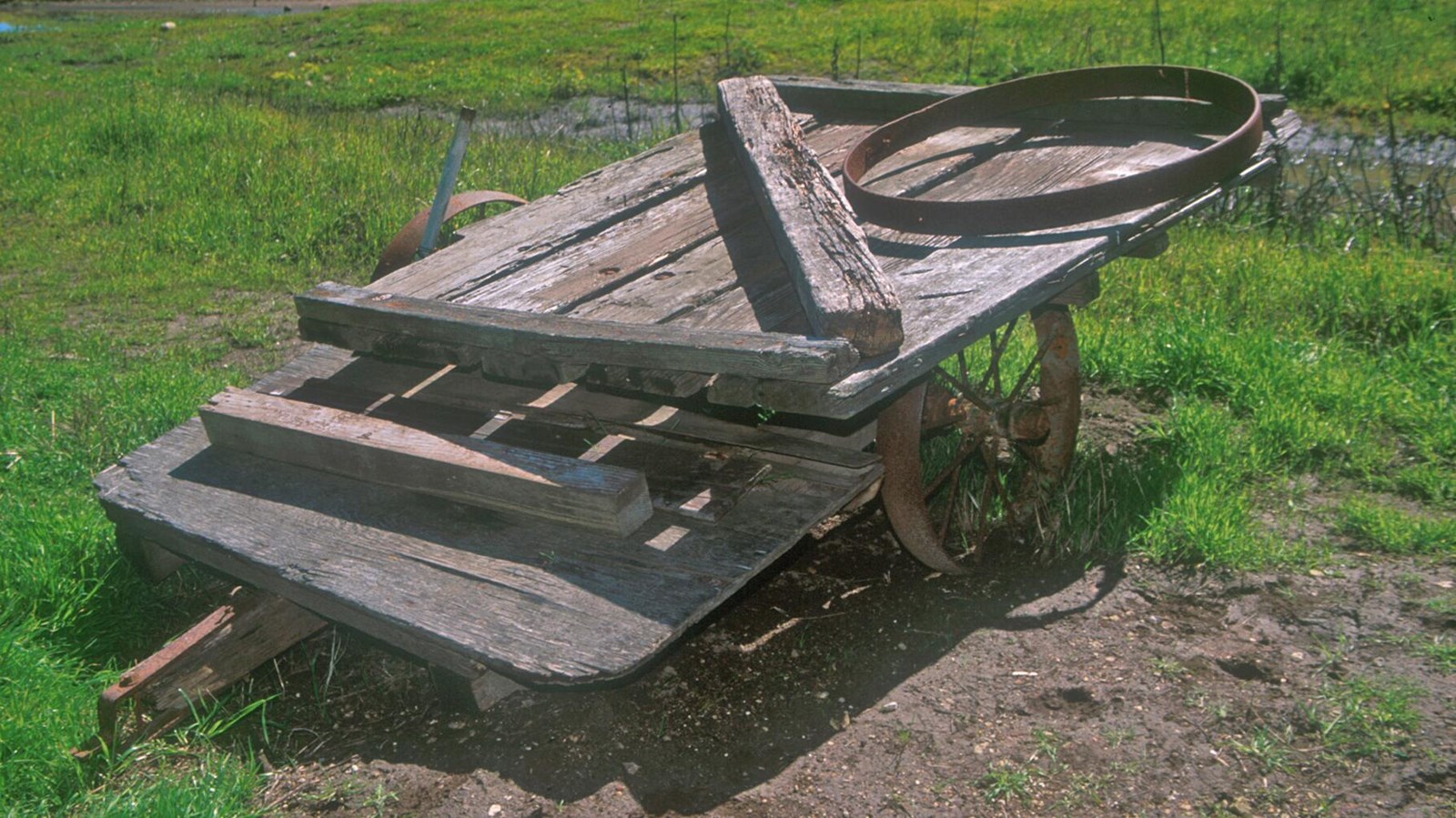 A wood framed wagon the size of a truck bed, the wood is bleached from the weather, rusted tire rims