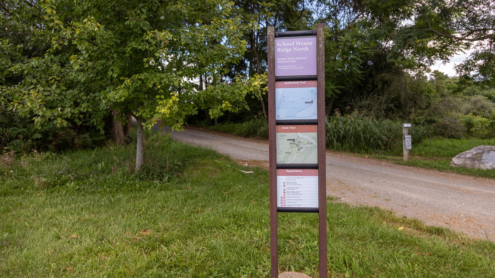 A tall, narrow signpost by a gravel road labeled
