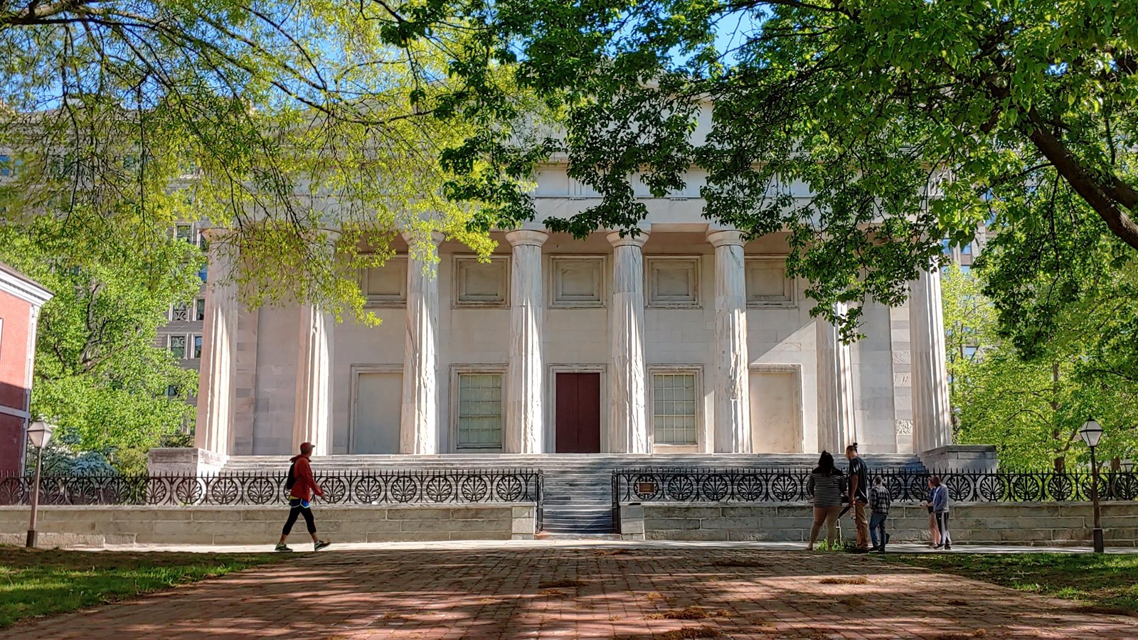 A color photo of a red brick path leading to a white marble building with tall columns.