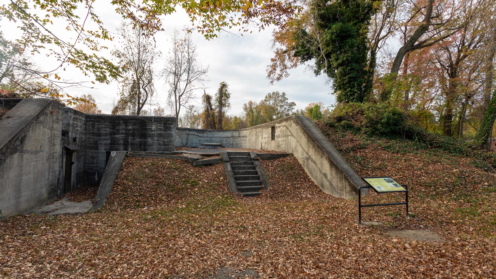 A concrete wall is constructed low to the ground. Concrete steps lead to the building.