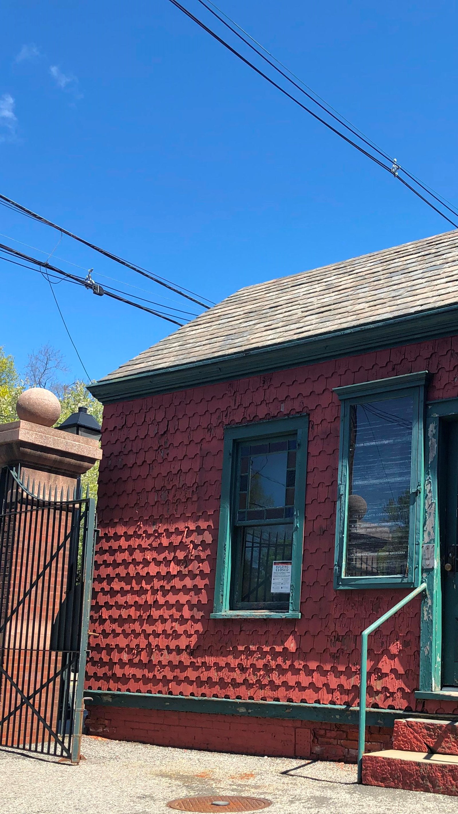 Exterior of painted red shingled house with green trim a slate roof and a small staircase to a door.