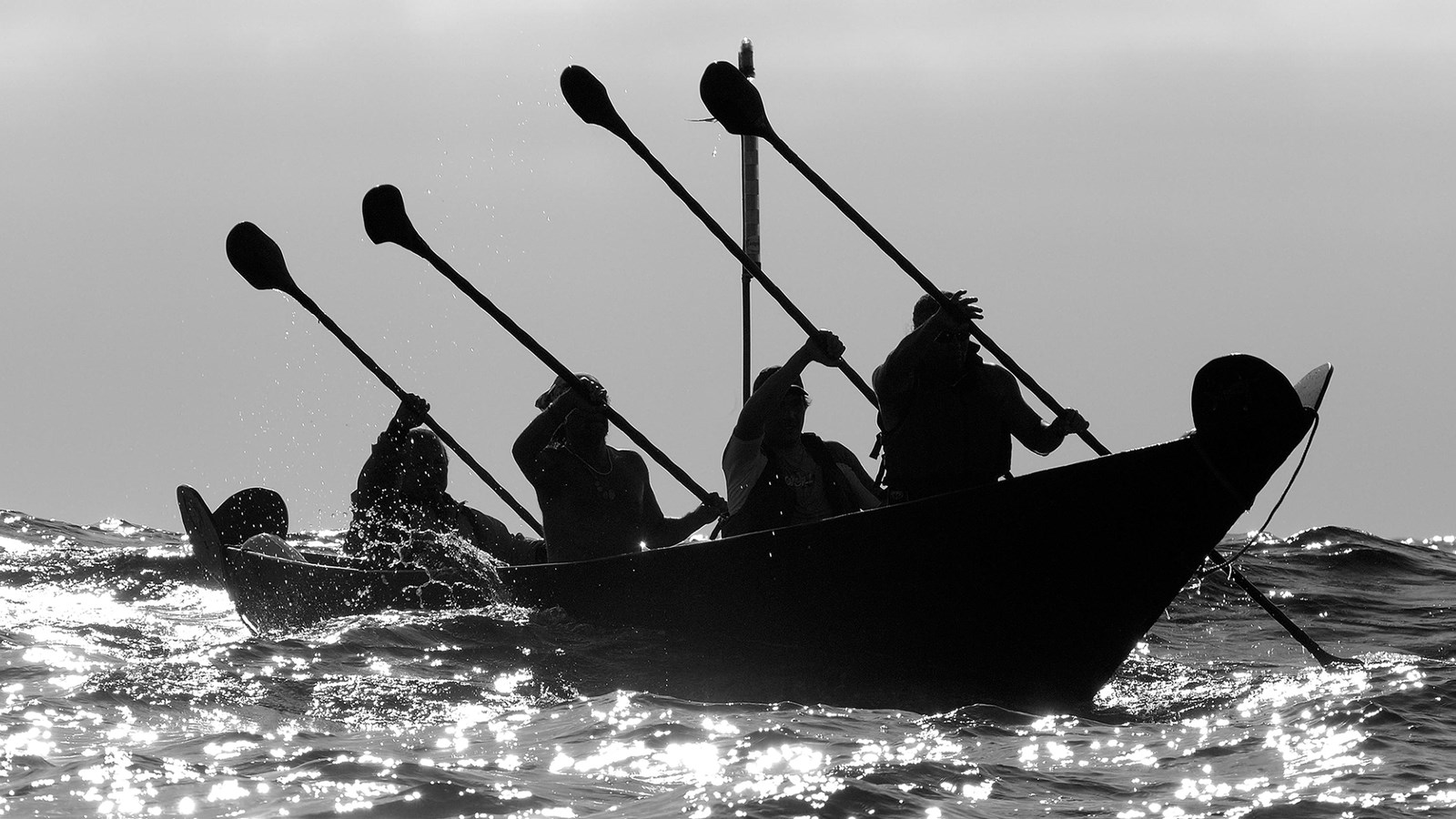 canoe shaped boat being paddled over the ocean.