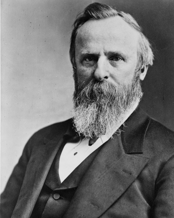 An 1800s half-length portrait photo depicts a seated man with a beard, facing left.