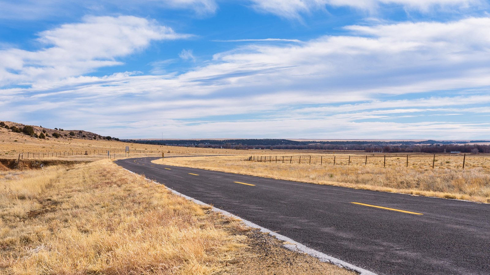 A two lane road stretches into the distance of a grassy area.