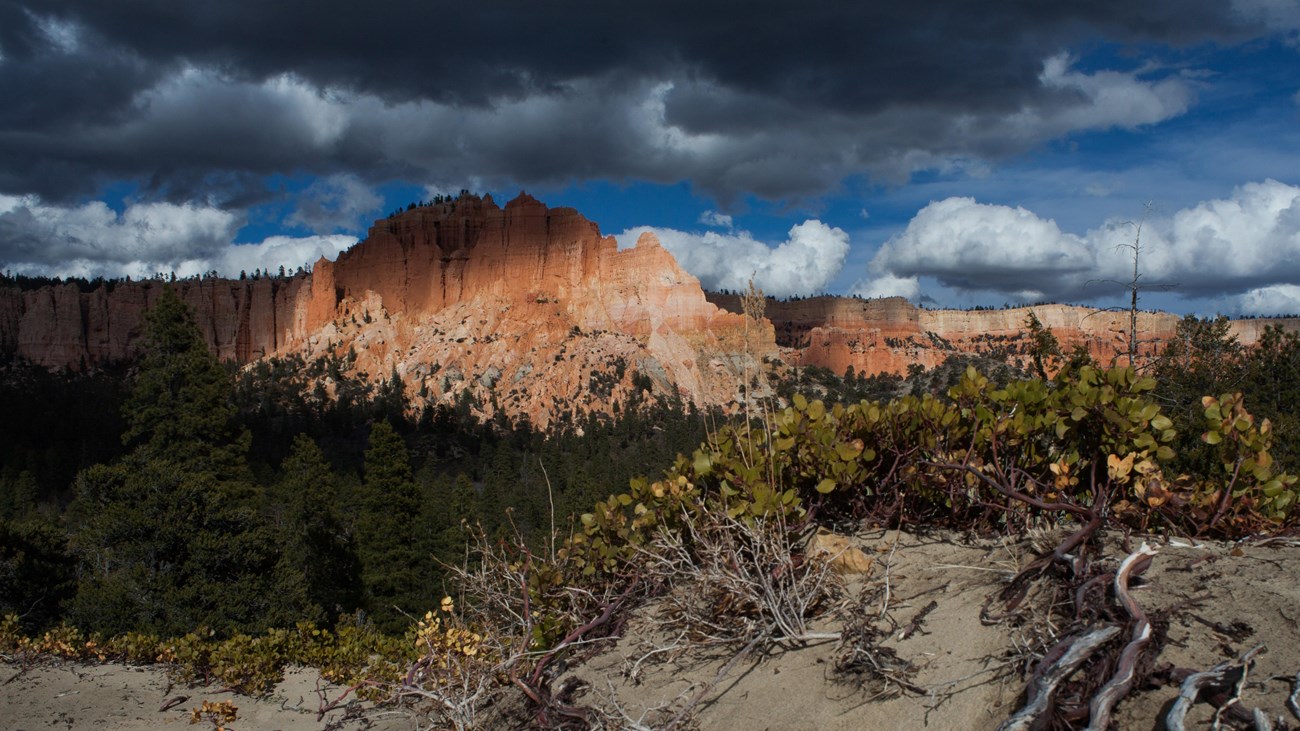 A large formation of red rock partially in shadow with threatening storm clouds above it