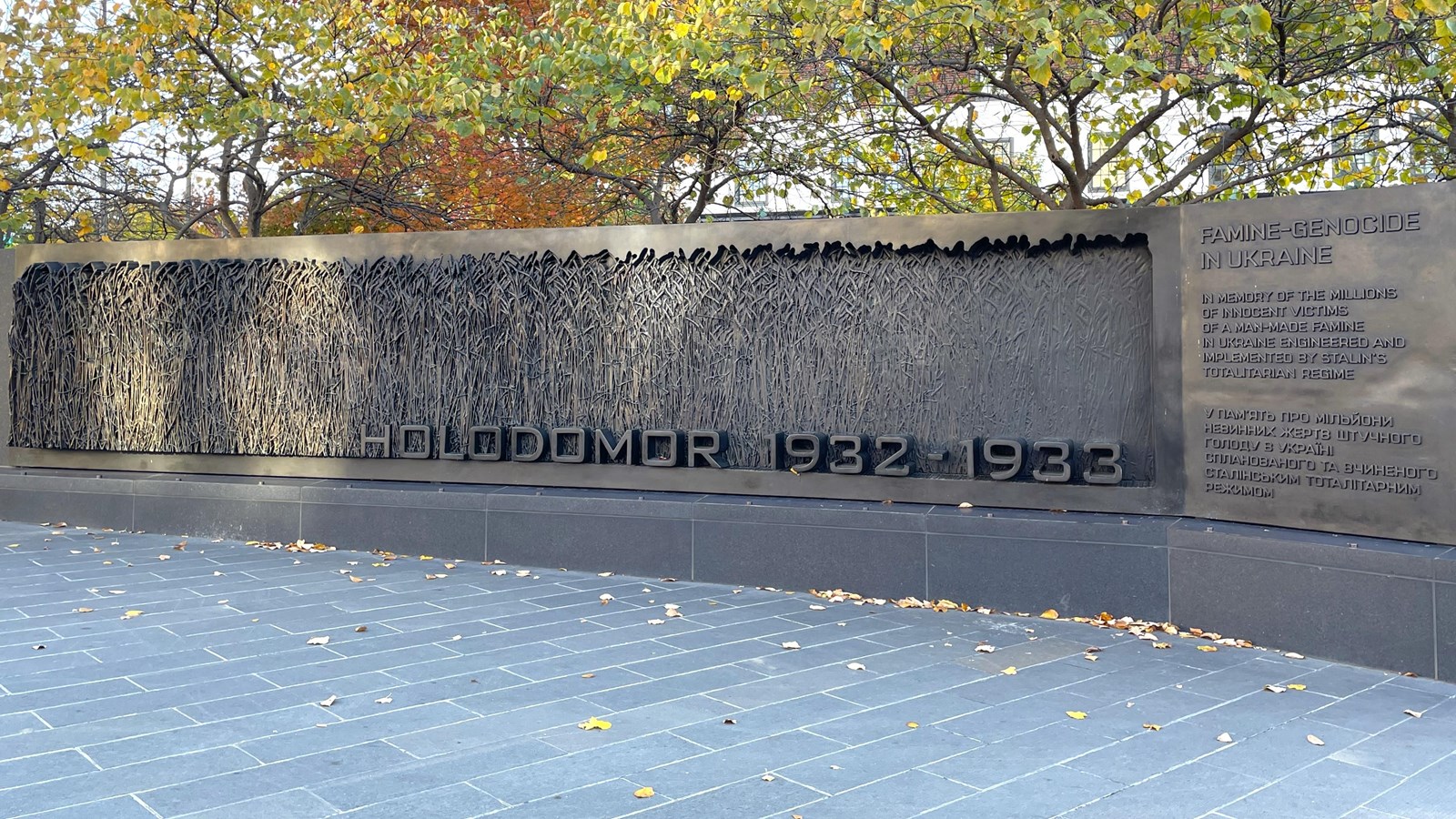 A horizontal bronze wall on a plaza of stone pavers