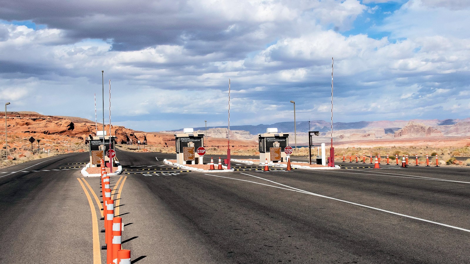 Asphalt road with orange cones along center lane. Three windowed booths in a row with arrowhead logo