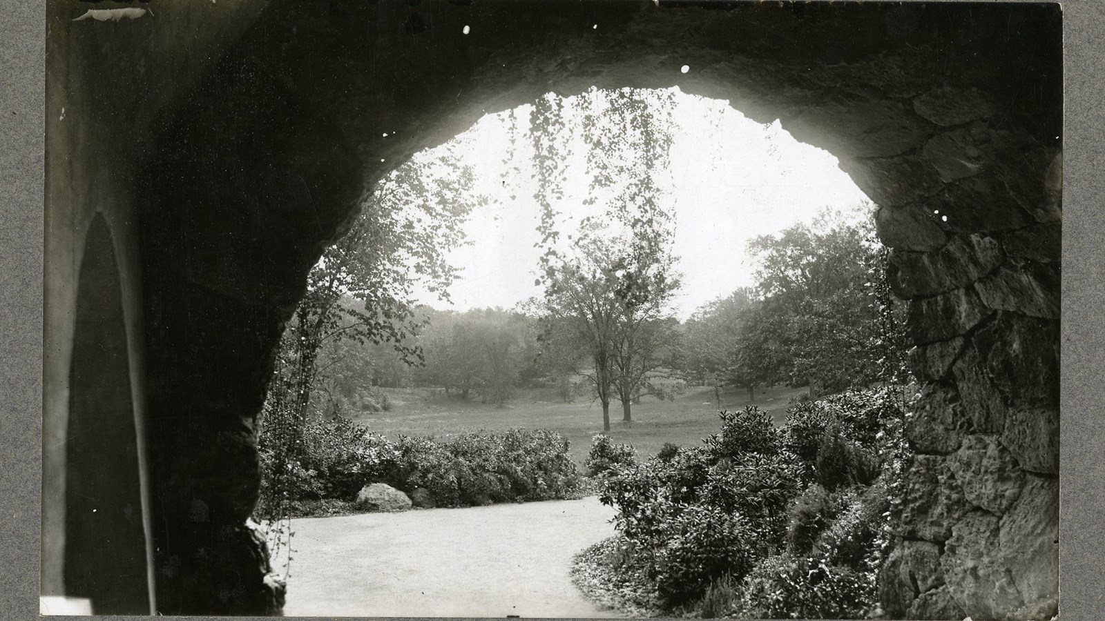 Black and white of arch looking out on grassy area with trees on edges of area