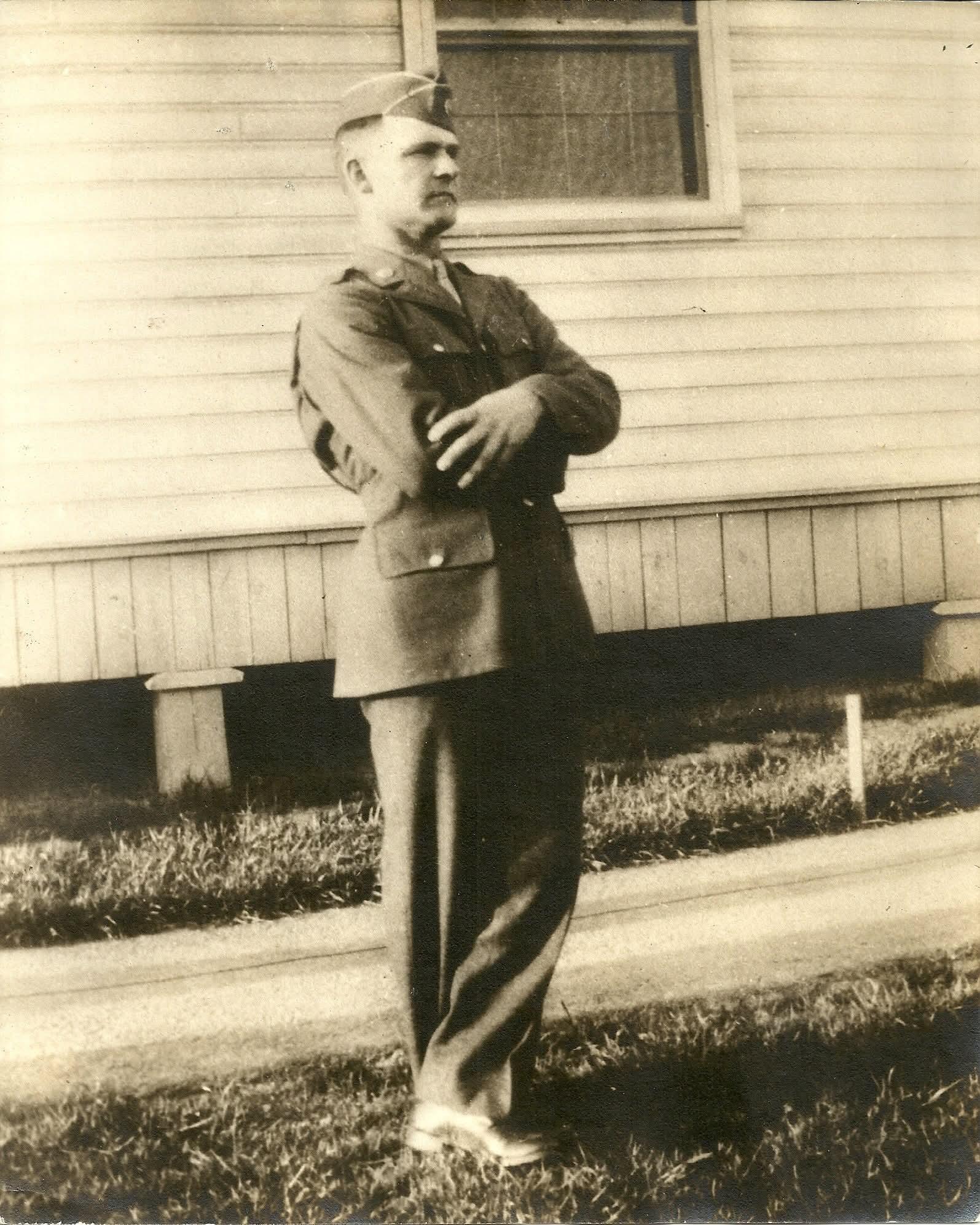 Young man wearing World War II dress uniform and hat posing for black and white photo. 