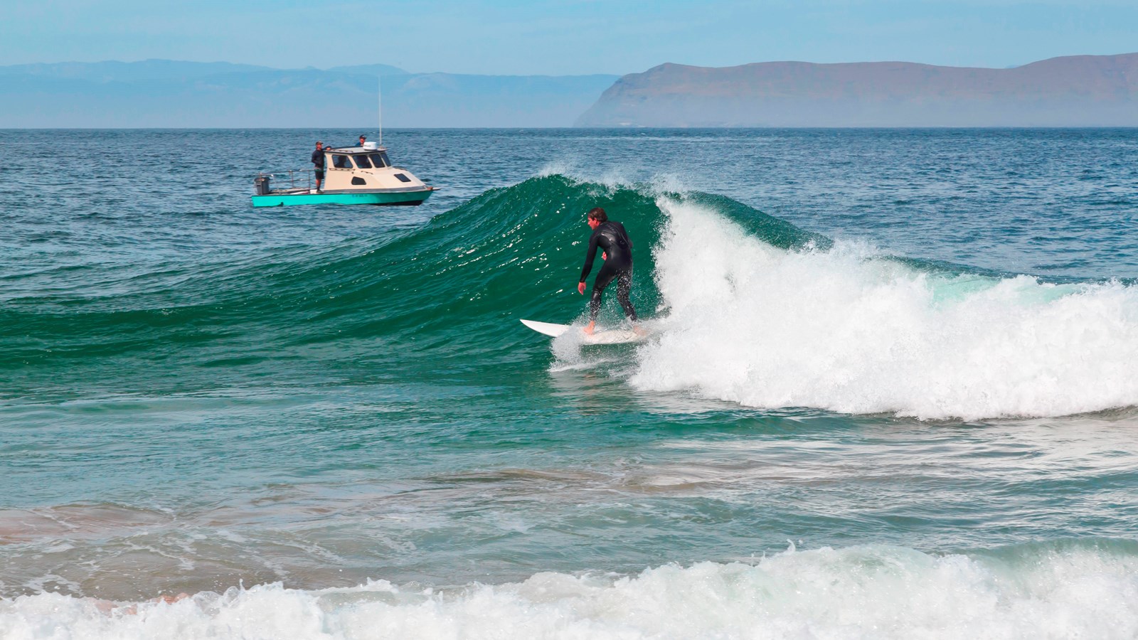surfer on wave with boat in background