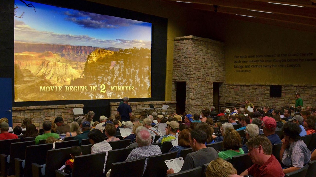 People are almost filling the seats in a darkened theater. Screen reads: Movie begins in 2 minutes.