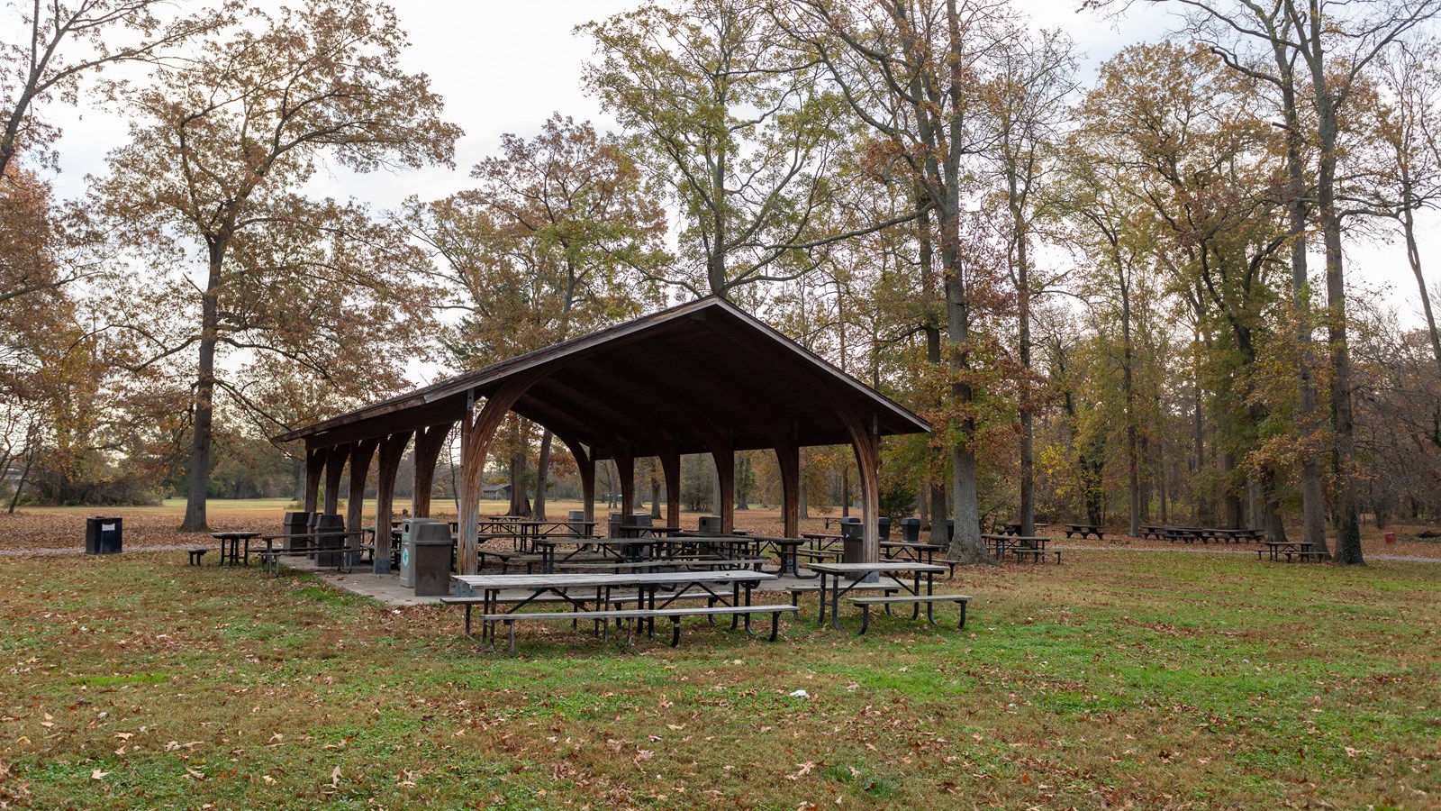 A picnic shelter has a roof, but no walls. Tables are under and outside of the pavilion.