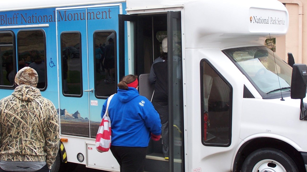 A passenger boards a shuttle bus, while another waits for his turn.