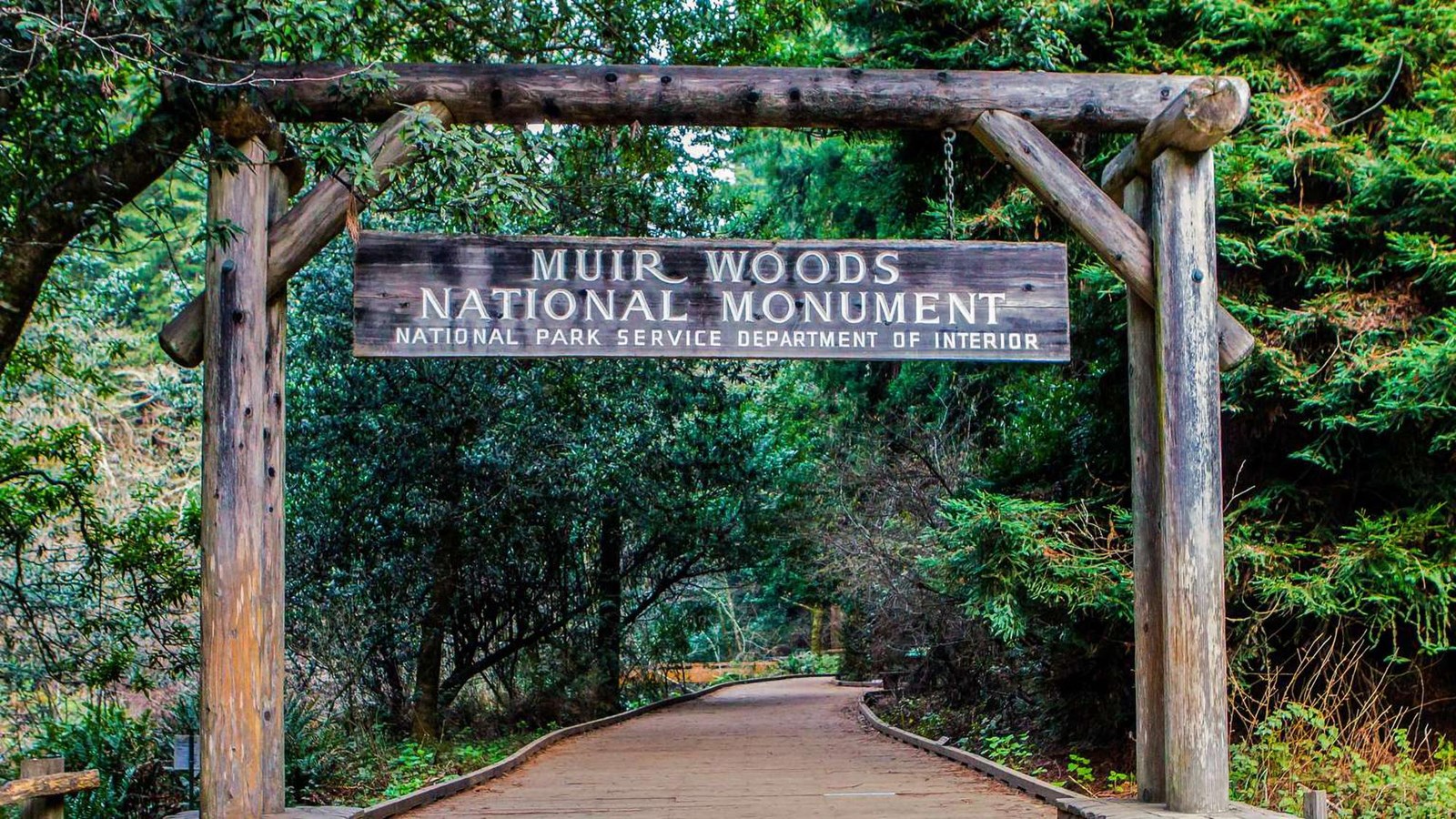 Wooden entrance gate. A wooden sign with the name of the park hangs from the gate. 