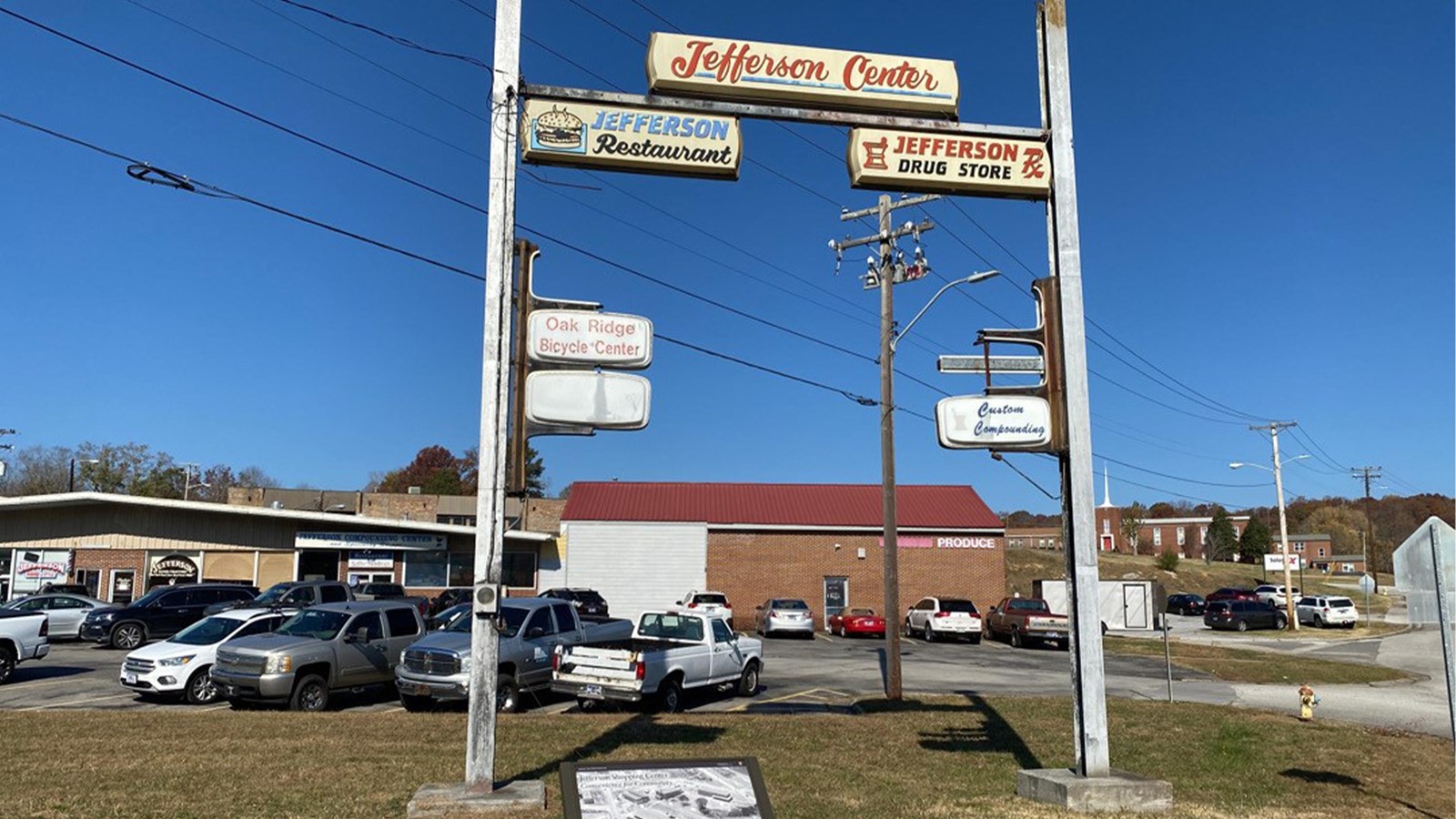 A large business sign in front of a strip mall. A wayside exhibit is visible in the foreground.