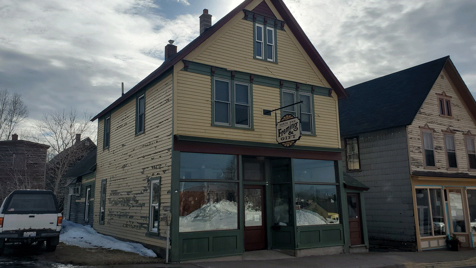 Two story wood-frame building with yellow wood siding and gabled roof. Sign reads North End Framing.