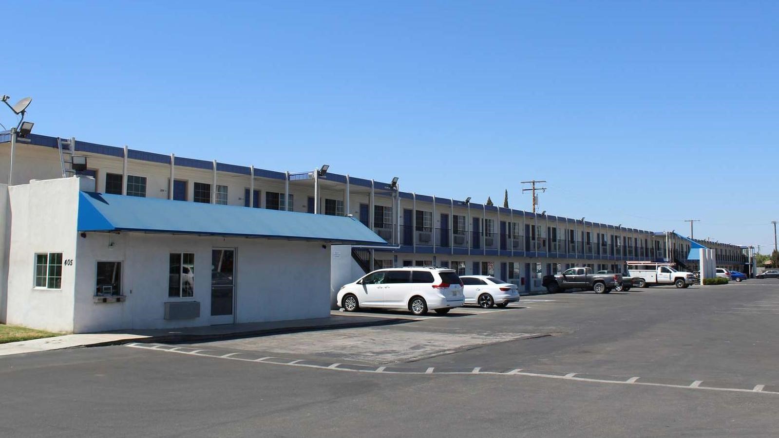 A long, low motel building with many rooms and a large parking area