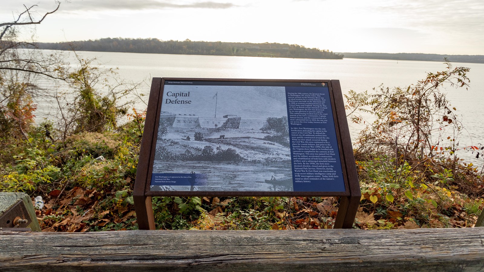 An information panel is positioned directly behind a wood barrier. A body of water is in the back.