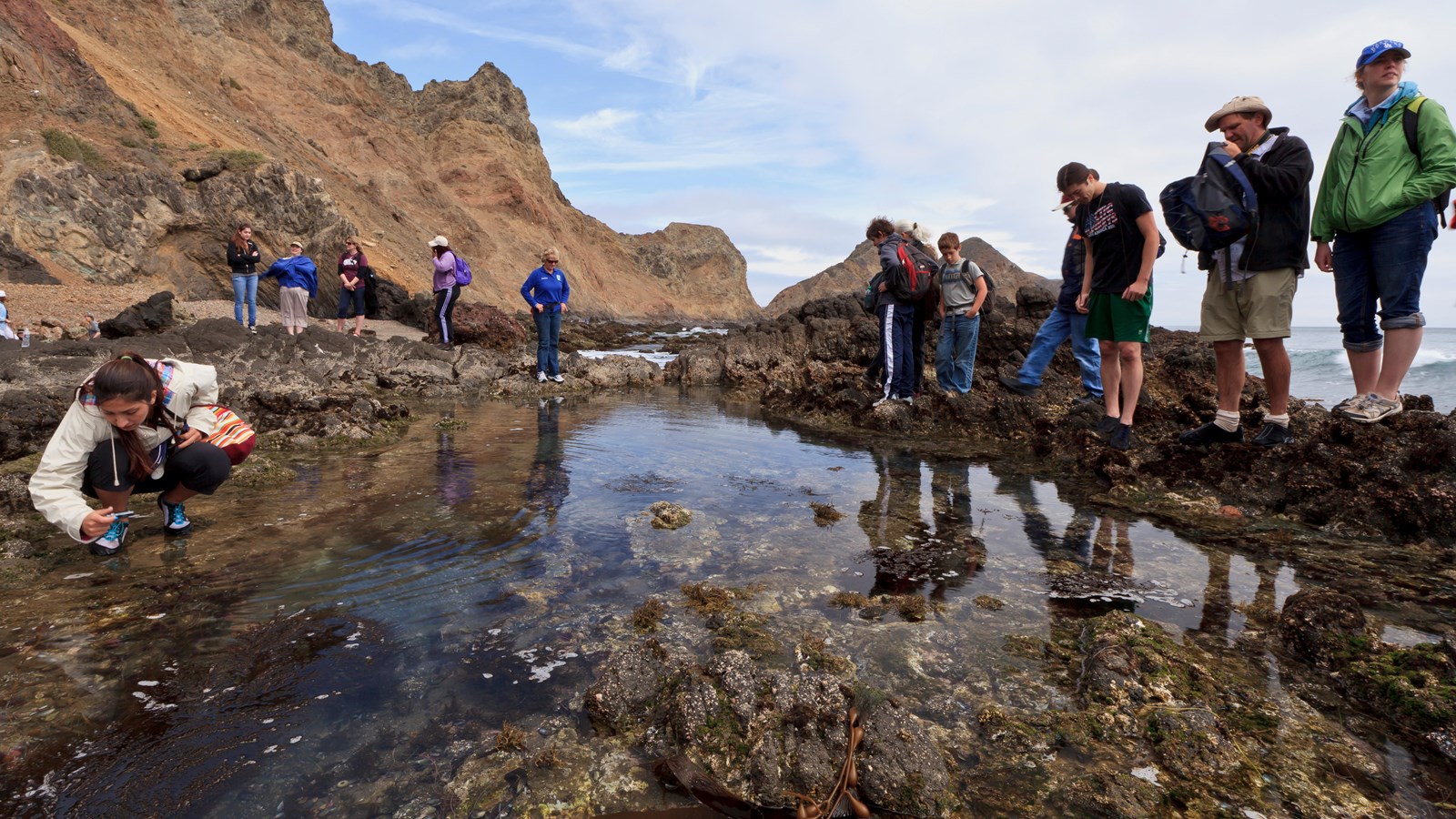 visitors at rocky pool along coast with steep cliffs