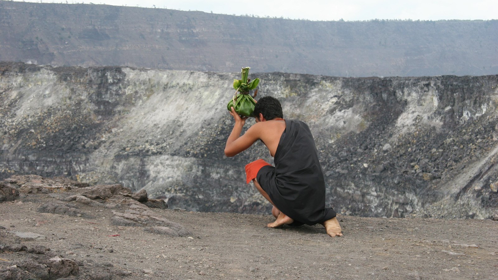Hawaiian cultural practitioner throwing an offering into a crater.