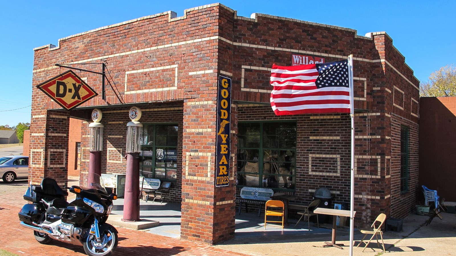 A red brick building with an extended porch covering. Under the cover are two old gas pumps.